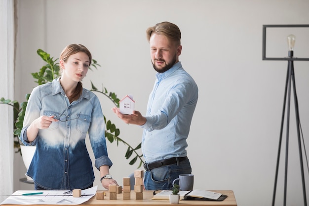 Free photo woman looking at small house model holding by her colleague at workplace