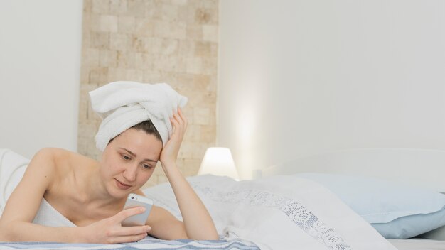 Woman looking at smartphone in bed after shower