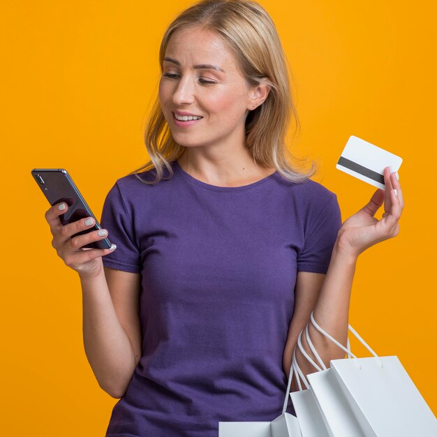 Woman looking at smartphone while holding credit card and shopping bags