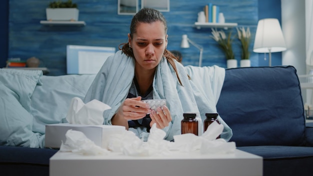 Free Photo woman looking at tablets of capsules and jar of pills on table finding healing treatment against headache and seasonal cold. unhappy person with sickness reading medicine labels