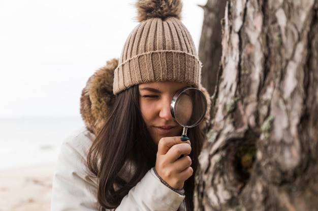 Woman looking at tree bark through magnifying glass