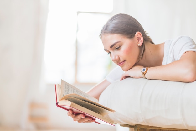 Woman lying on bed reading book at home