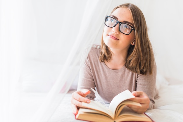 Woman lying on bed with book daydreaming