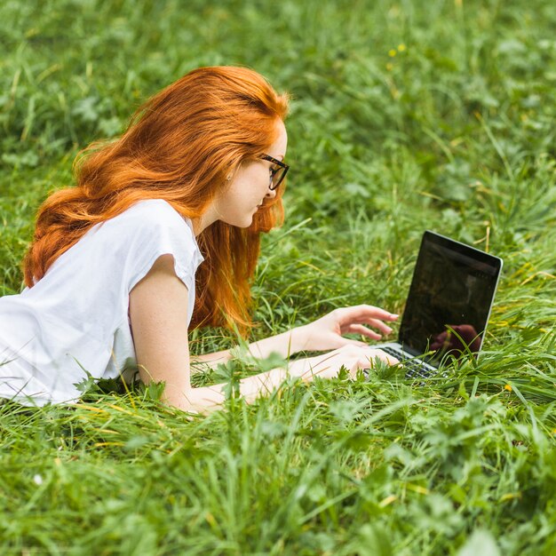 Free Photo woman lying on grass with laptop 