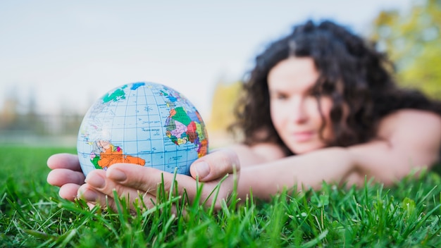 Free photo woman lying on green grass holding globe in hand over green grass