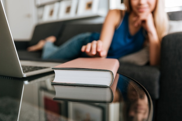 Free Photo woman lying on sofa and taking book from the table