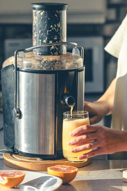 Free photo a woman makes orange juice at home in the kitchen with an electric juicer