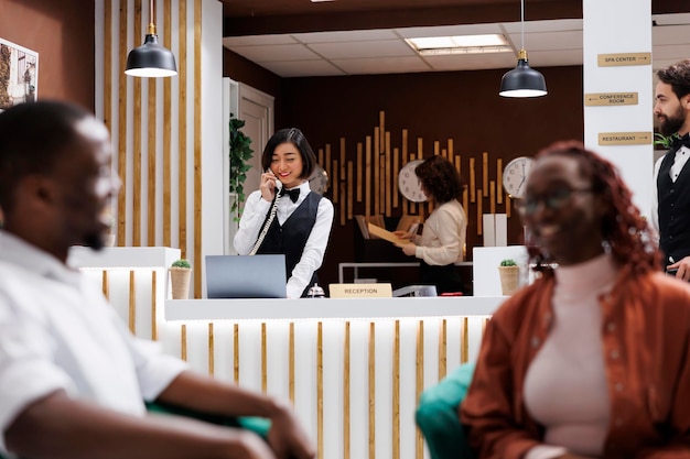 Woman making online booking on phone, talking on landline phone call to check room availability for new reservation. Female receptionist giving assistance to future hotel guests.