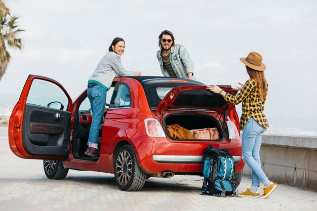 Woman and man leaning out from car near lady with backpack near car trunk