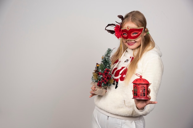 Woman in masquerade mask holding gift and pinetree.