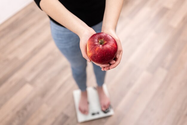 A woman measures weight on a scale holds an apple in her hands