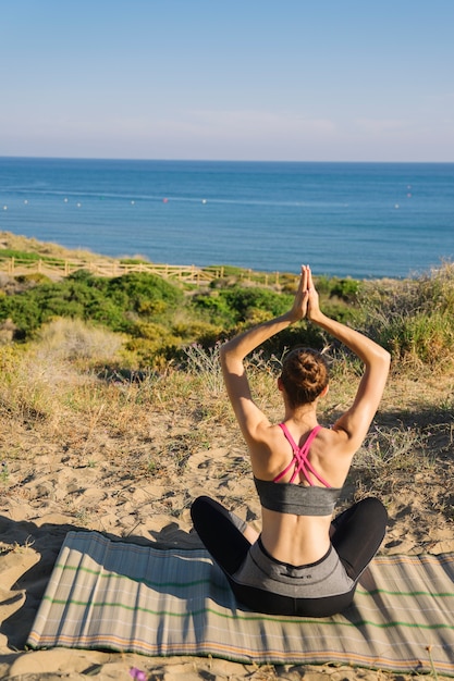 Free photo woman meditating at the beach back view