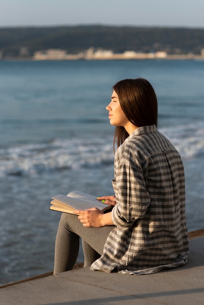 Free photo woman meditating and reading on the beach