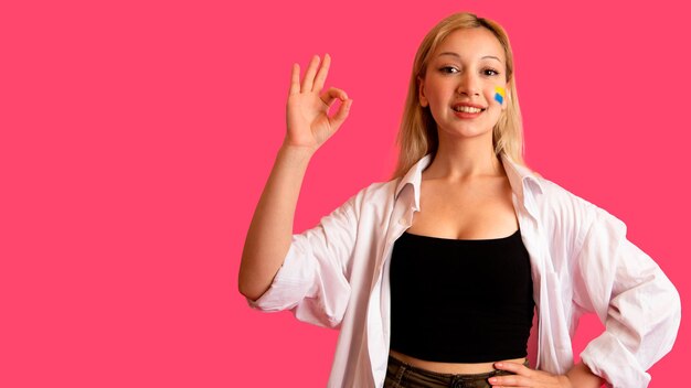 Woman of model appearance with the flag of Ukraine on her face holds posing on a pink background