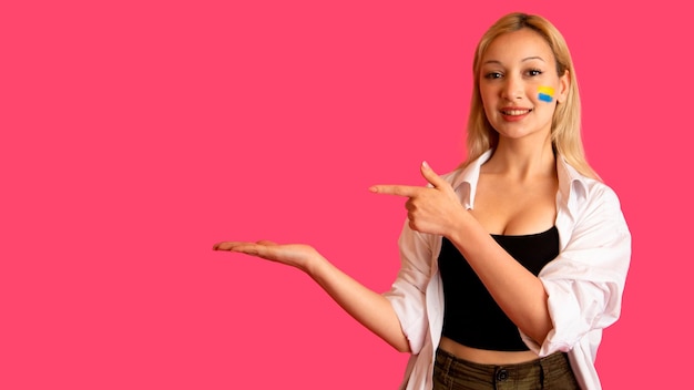 Woman of model appearance with the flag of Ukraine on her face holds posing on a pink background