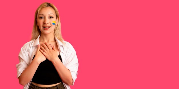 Woman of model appearance with the flag of Ukraine on her face holds posing on a pink background