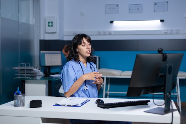 Woman nurse using video call with webcam on computer for remote conversation, working late. Medical assistant talking to patient on online video conference for telehealth and consultation