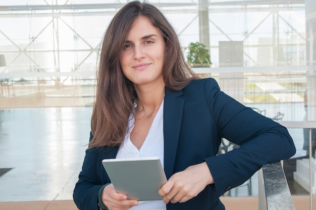 Woman in office looking at camera, holding tablet in hands