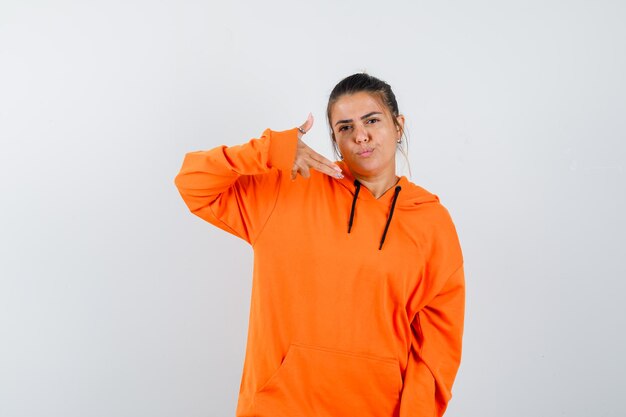 Woman in orange hoodie showing gun gesture and looking confident