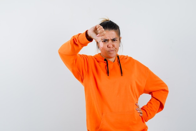 Woman in orange hoodie showing thumb down and looking gloomy