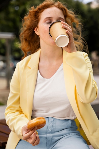 Free Photo woman outdoors enjoying a tasty donut and a cup of coffee