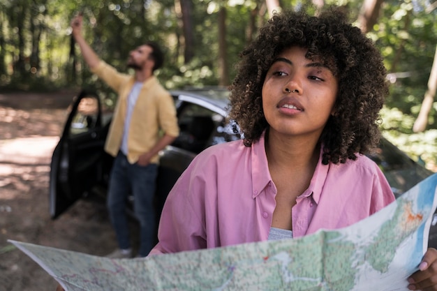 Free photo woman outdoors holding map while boyfriend takes selfie next to car