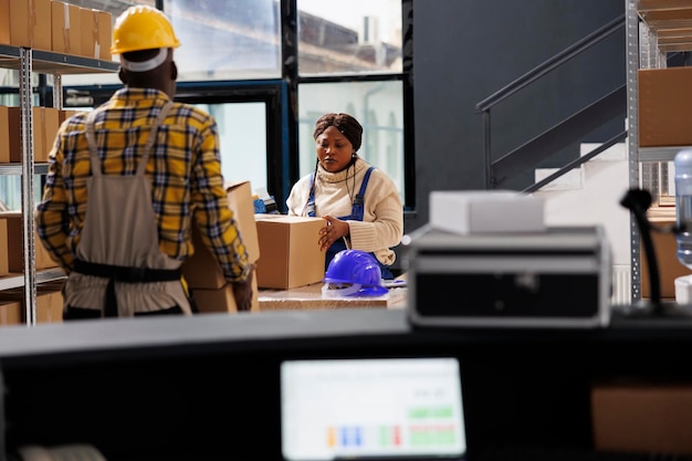 Free photo woman package handler putting cardboard box on table and preparing parcel before shipment in warehouse. deliver service african american worker packing carton in storage room