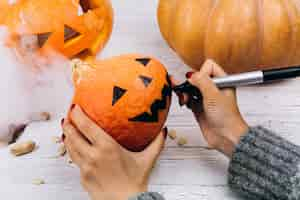 Free photo woman paints a face on a little orange pumpkin for halloween