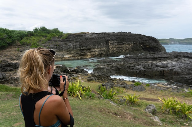 Free photo woman photographer traveler photographing landmarks on camera,  angel's billabong beach, nusa penida island, bali, indonesia.