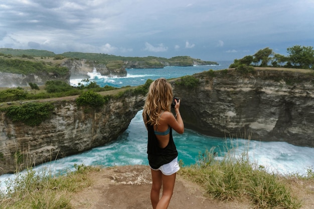 Free Photo woman photographer traveler photographing landmarks on camera,  angel's billabong beach, nusa penida island, bali, indonesia.