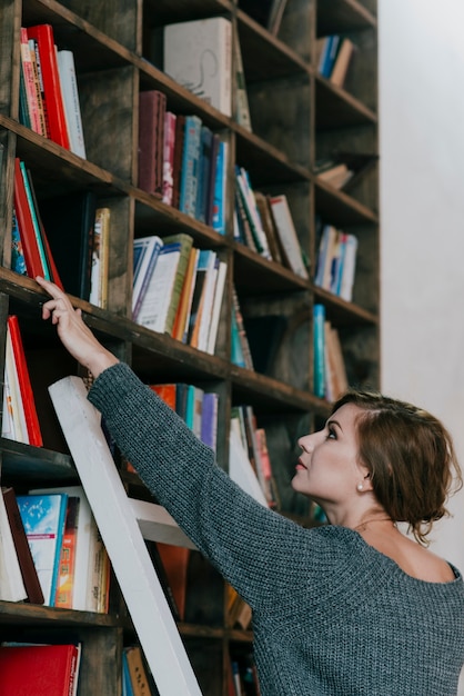 Free Photo woman picking book from bookshelf