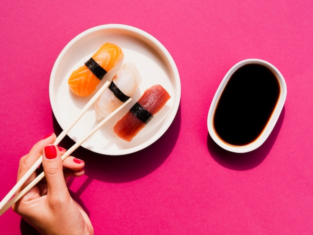 Woman picking a sushi from plate with chop sticks