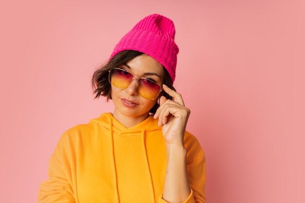 Free photo woman in pink hat and orange hoodie posing on pink . stylish sunglasses.