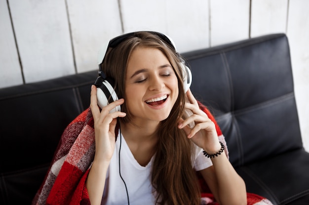 Free Photo woman in plaid listening music in headphones, sitting on sofa.