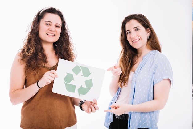 Free photo woman pointing to recycle placard hold by her friend against white backdrop