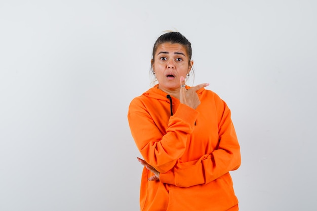 woman pointing to the right side in orange hoodie and looking surprised