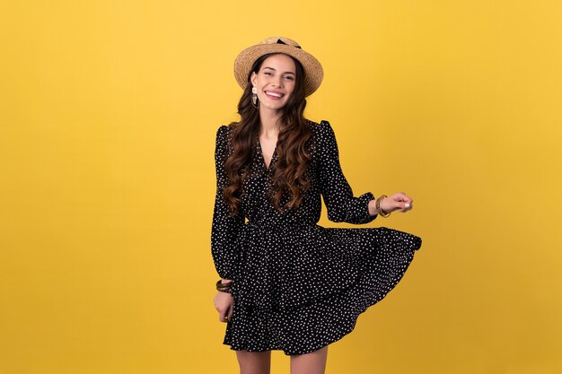 woman posing isolated on yellow wearing black dotted dress and straw hat stylish boho