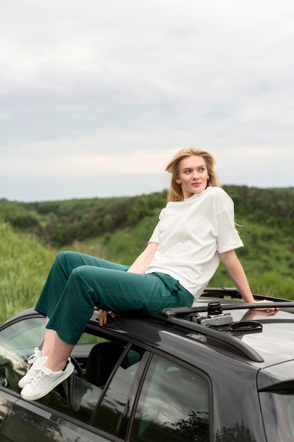 Free photo woman posing in nature while standing on top of car