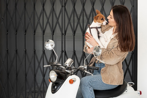 Free Photo woman posing on scooter while holding her dog