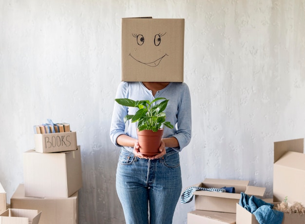 Free photo woman posing while holding plant in hand and box over head on moving day