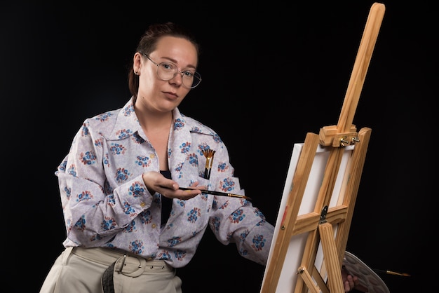 Woman posing with brushes and canvas on black background . 