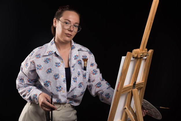 Woman posing with brushes and canvas on black . High quality photo