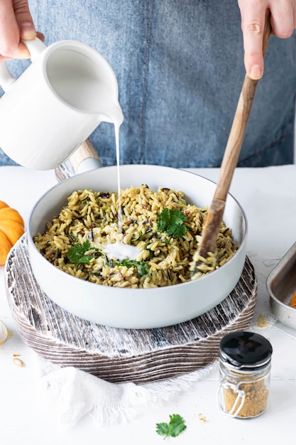 Free photo woman pouring coconut milk over curry rice and coriander