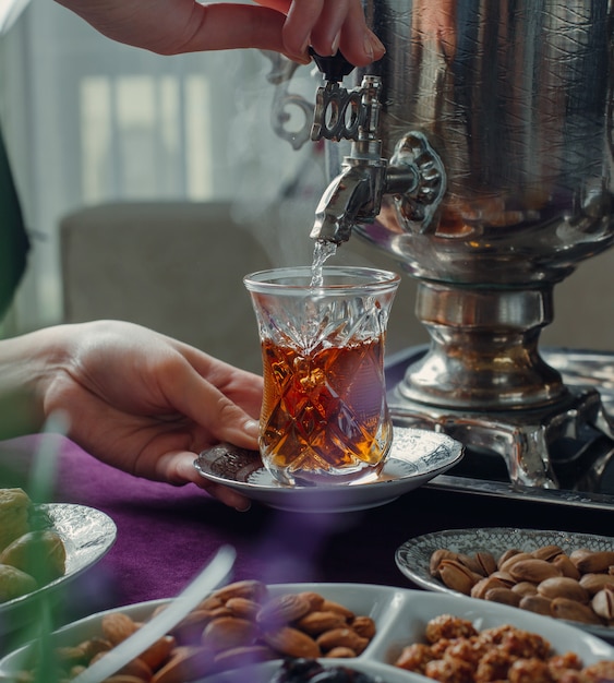 Free Photo woman pouring hot water into glass with black tea from samovar