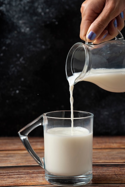 Woman pouring milk into the glass mug wooden table. 