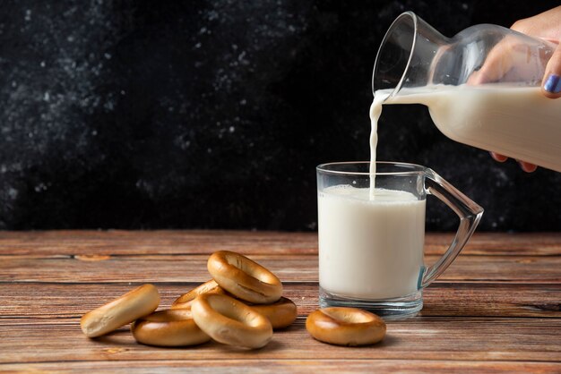 Woman pouring milk into the glass and round biscuits on wooden table. 