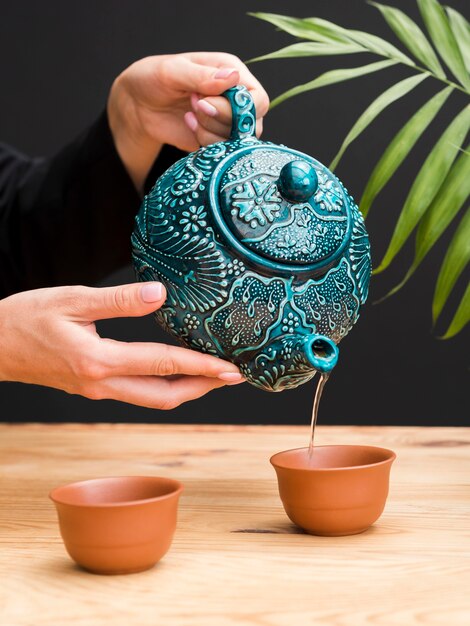 Woman pouring tea in clay teacup with teapot