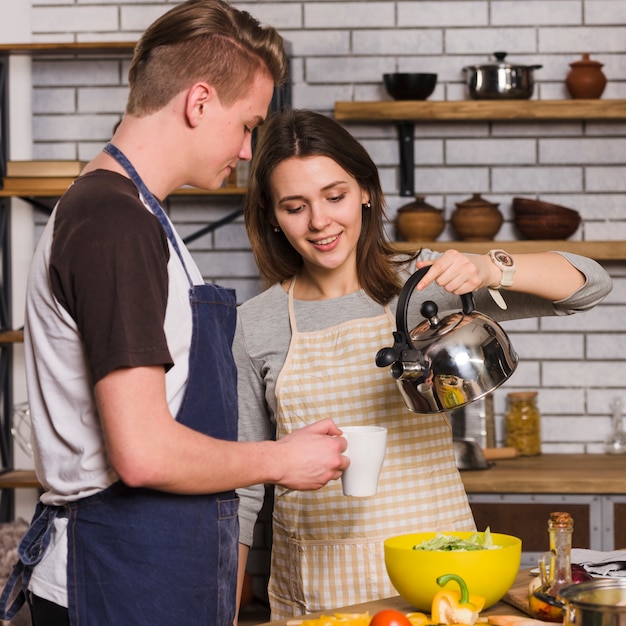 Woman pouring water from kettle into mug for man