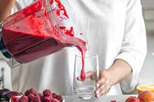 Free photo a woman pours a berry smoothie from a blender into a glass