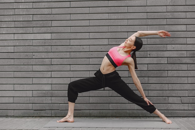 Woman practicing advanced yoga against a dark urban wall